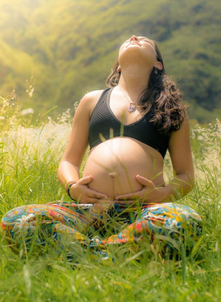 woman holding her pregnant stomach looking up to the sun - yoga during pregnancy